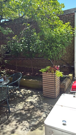 Un patio con pared de ladrillo, una mesa de metal con sillas y una jardinera con plantas.