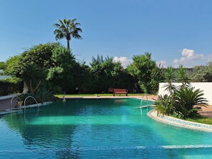 A clear swimming pool with a palm tree and benches in the background. - La Perla Azure3br Pool - 12-min Walk to the Beach (Hammamet)
