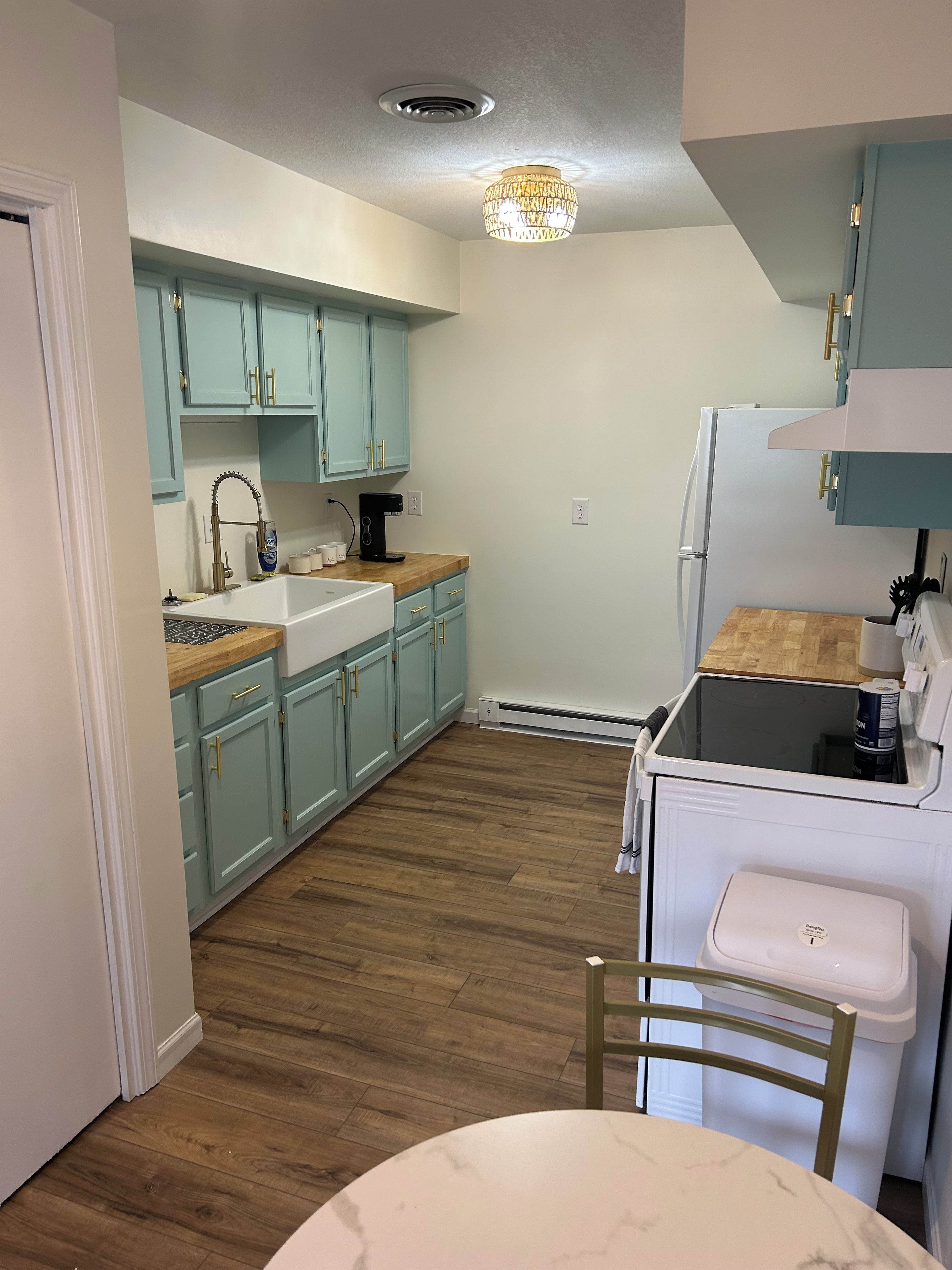 A compact kitchen with light blue cabinets, a white refrigerator, a coffee maker, and a dining table with a chair.