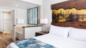 Una habitación de hotel con cama, mesita de noche, escritorio, ducha y obras de arte en las paredes.