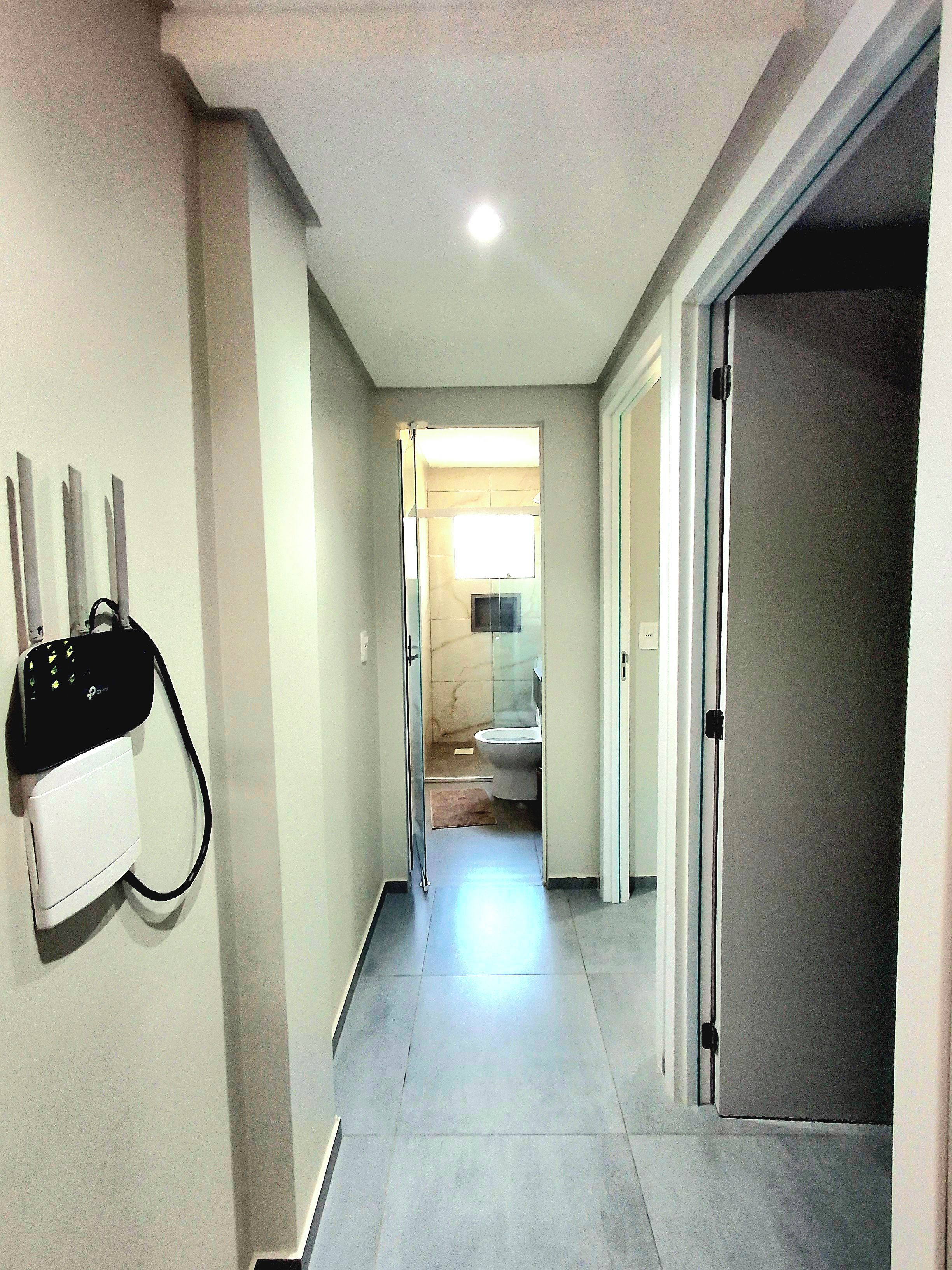 Un pasillo con un enchufe de pared, una puerta que da a un baño y un suelo de baldosas.
