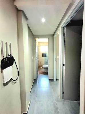 Un pasillo con un enchufe de pared, una puerta que da a un baño y un suelo de baldosas.