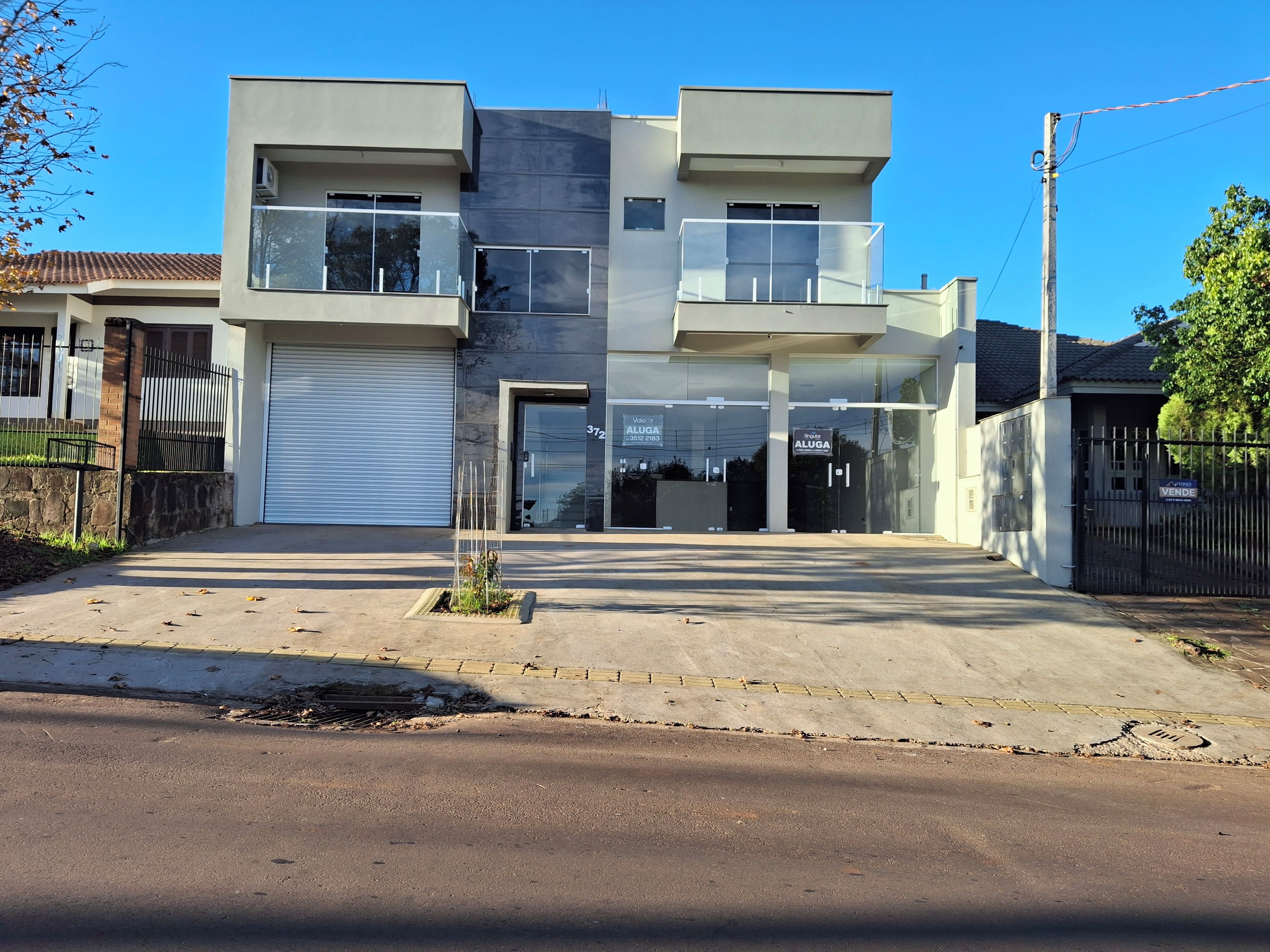 Un edificio moderno de dos pisos con puerta de garaje, balcón y entrada protegida por una reja.