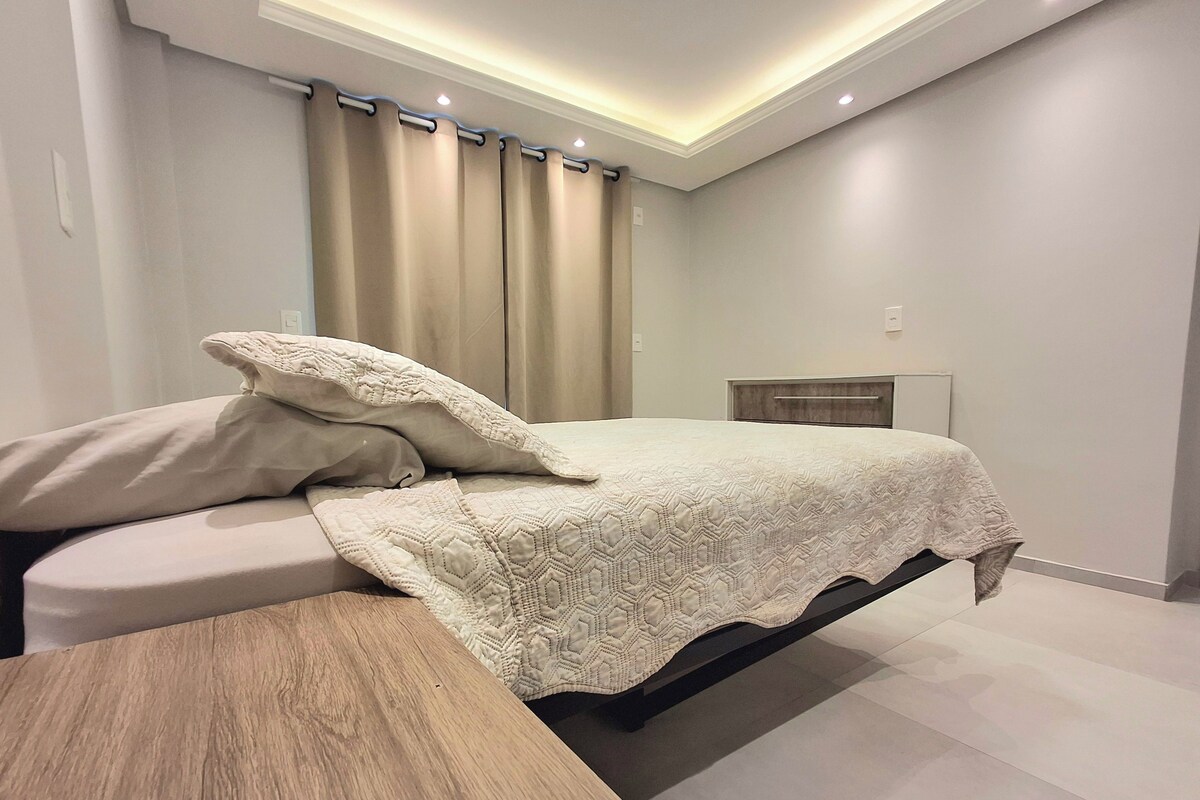 Un dormitorio moderno con cama, mesita de noche y cortinas.