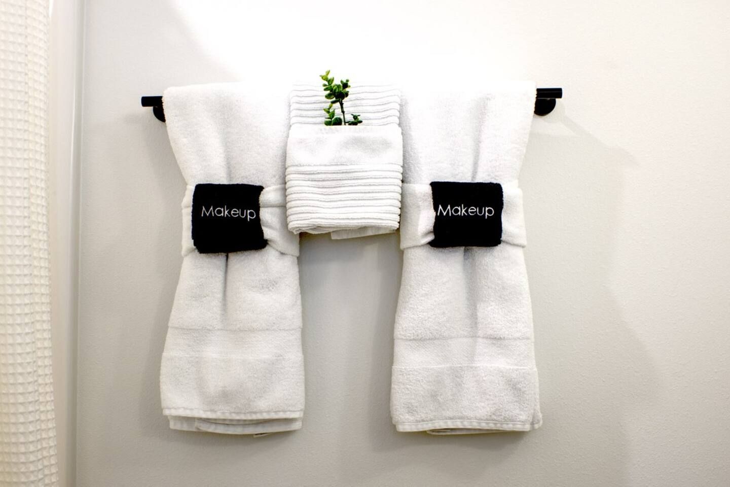 A bathroom with two white towels hanging on a wall-mounted towel rack, each with a black tag labeled 'Makeup'.