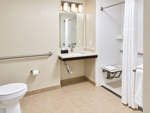 Et badeværelse med toilet, vask, spejl, håndklædestang og bruseområde.