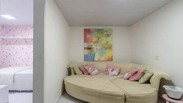 Een kamer met een beige bank, een kleurrijk abstract schilderij en een roze behang.