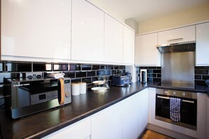 A modern kitchen with white cabinets, a black countertop, a built-in oven, and a microwave. - 2BR House Nr Etihad l Parking/Garden/Pool Table (Manchester)