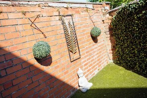 A brick wall with decorative elements including a metal leaf design, two spherical topiary plants, and a small Buddha statue. - 2BR House Nr Etihad l Parking/Garden/Pool Table (Manchester)