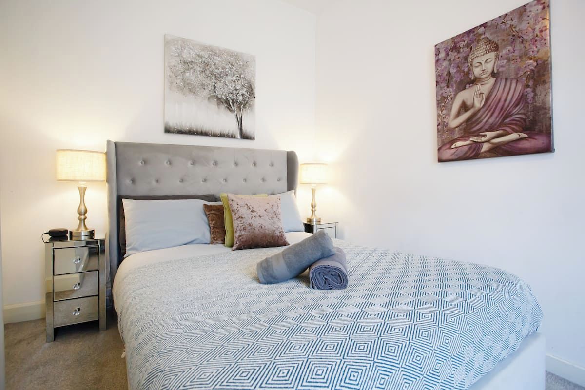 Un lit bien fait, avec une couvre-lit à motifs, une tête de lit et deux lampes de chevet.