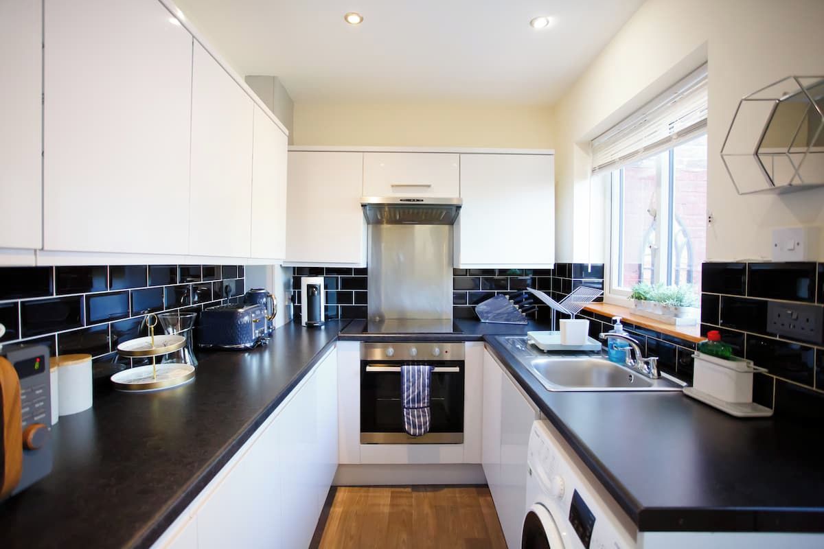 A modern kitchen with white cabinets, black countertops, a built-in oven, and a window providing natural light.