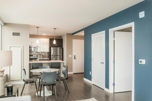 A modern kitchen with stainless steel appliances, a dining area with a round table and chairs, and a hallway with a blue accent wall and a white door.
