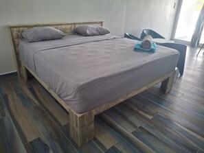 Een bed met houten frame en grijze beddengoed, een blauwe stoel en een raam met gordijnen.