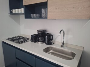 Een keuken met een gasfornuis, een koffiezetapparaat, een broodrooster en een spoelbak.