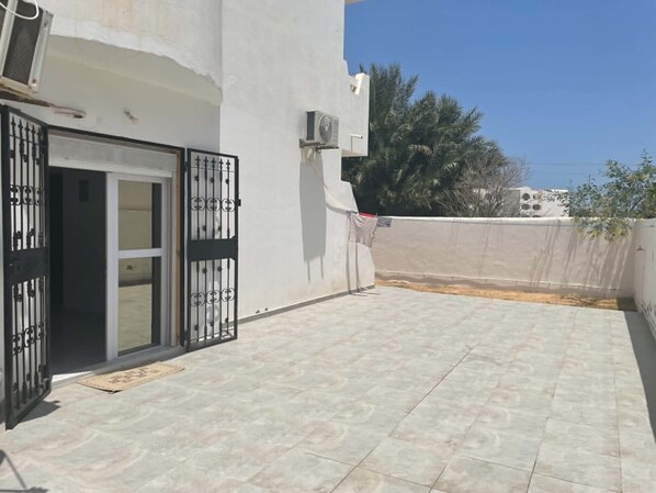 A rooftop terrace with a tiled floor, a sliding glass door, and a wall-mounted air conditioning unit. - New Listing (Djerba Midun)