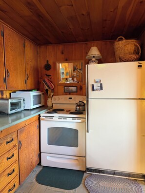 Cocina compacta con armarios de madera, microondas, estufa y refrigerador.