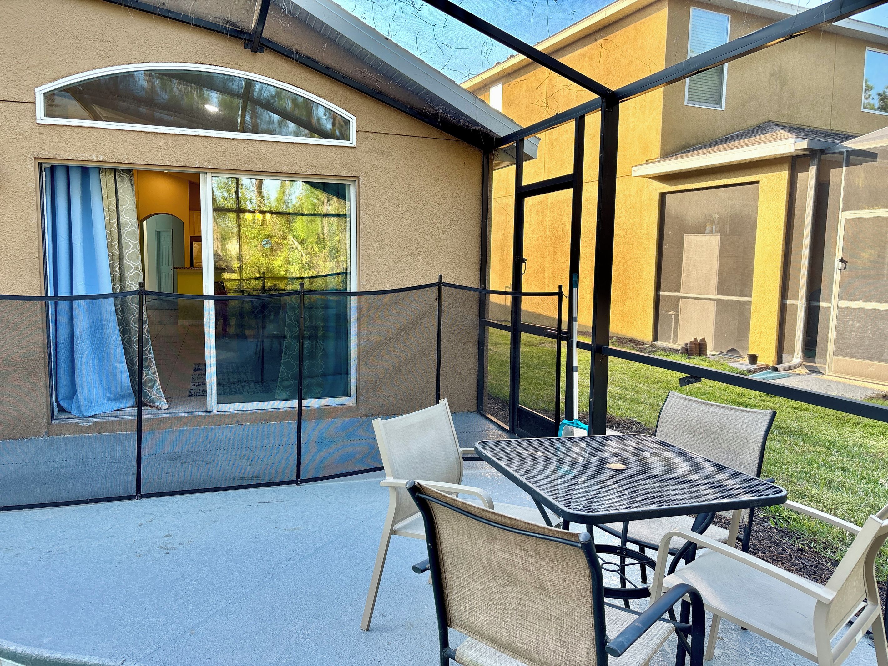 An outdoor patio with a table and chairs, a glass enclosure, and a view of a building with a garage.
