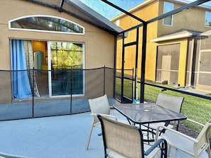 An outdoor patio with a table and chairs, a glass enclosure, and a view of a building with a garage.
