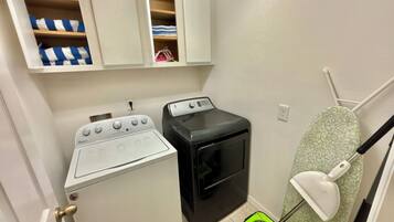 A laundry area with a Whirlpool washer and dryer, a small ironing board, and a mop.