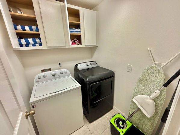 A laundry area with a Whirlpool washer and dryer, a small ironing board, and a mop.
