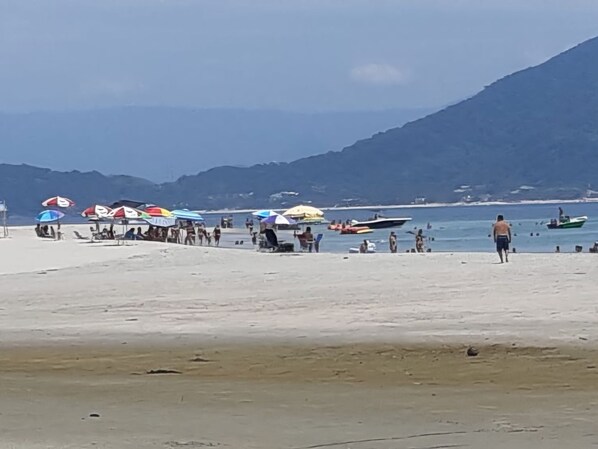 Ein Strand mit Sonnenschirmen, Booten und einer hügeligen Landschaft im Hintergrund.