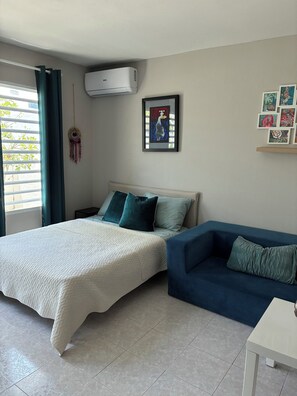 Una camera da letto con un letto, un divano, un condizionatore d'aria a parete e un portafortuna.