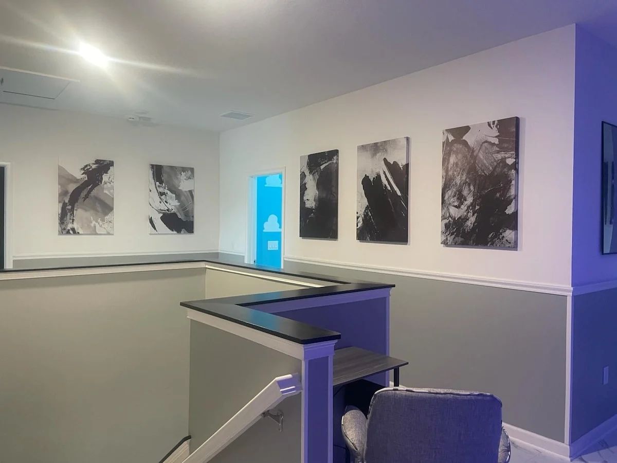 A room with a reception desk, a chair, and a wall with several abstract paintings.