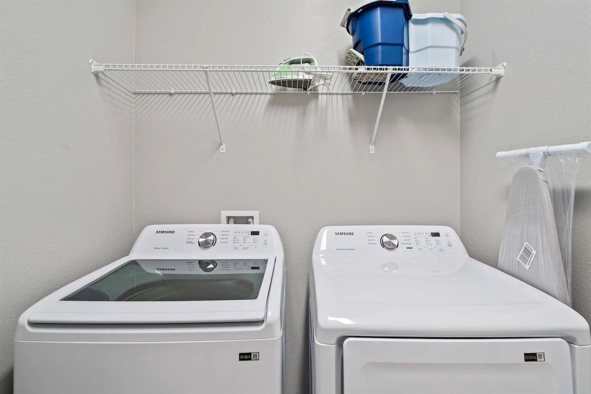A laundry area with two white Samsung washing machines and a metal shelf above them.