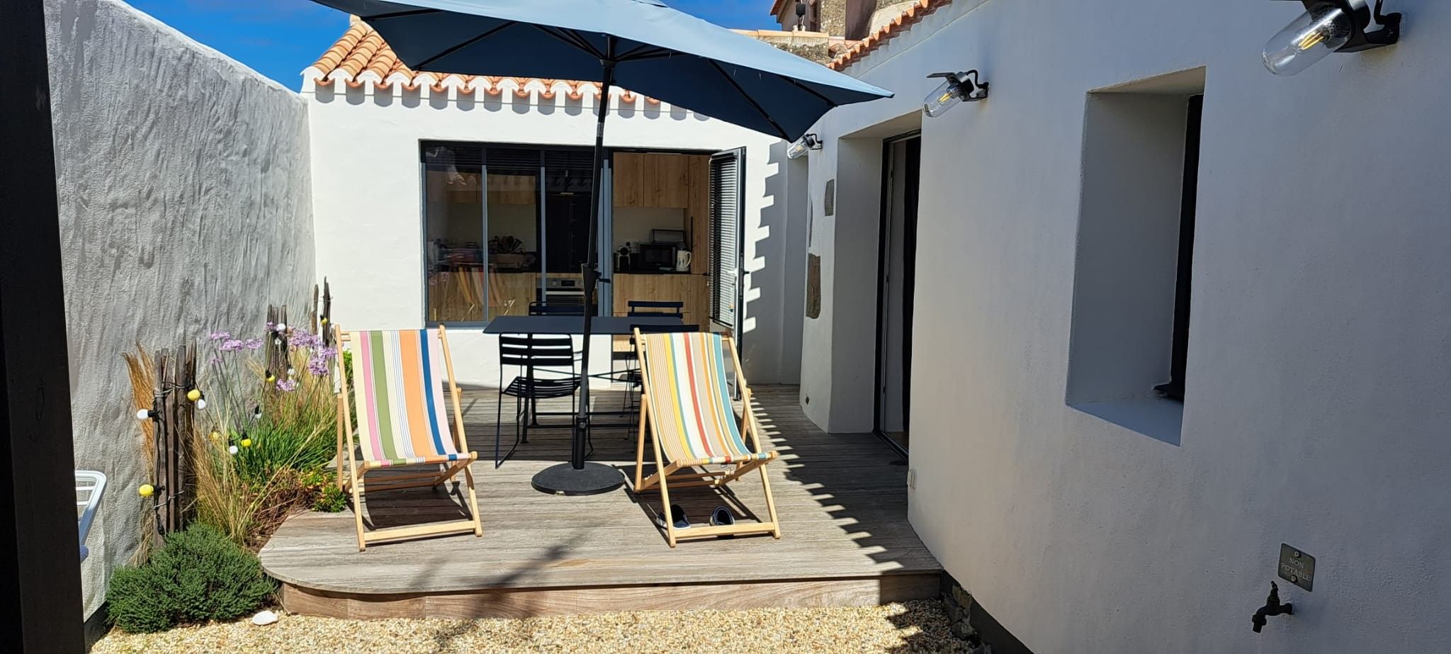A patio with two striped beach chairs, a table, and a large umbrella.