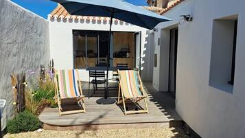 A patio with two striped beach chairs, a table, and a large umbrella.