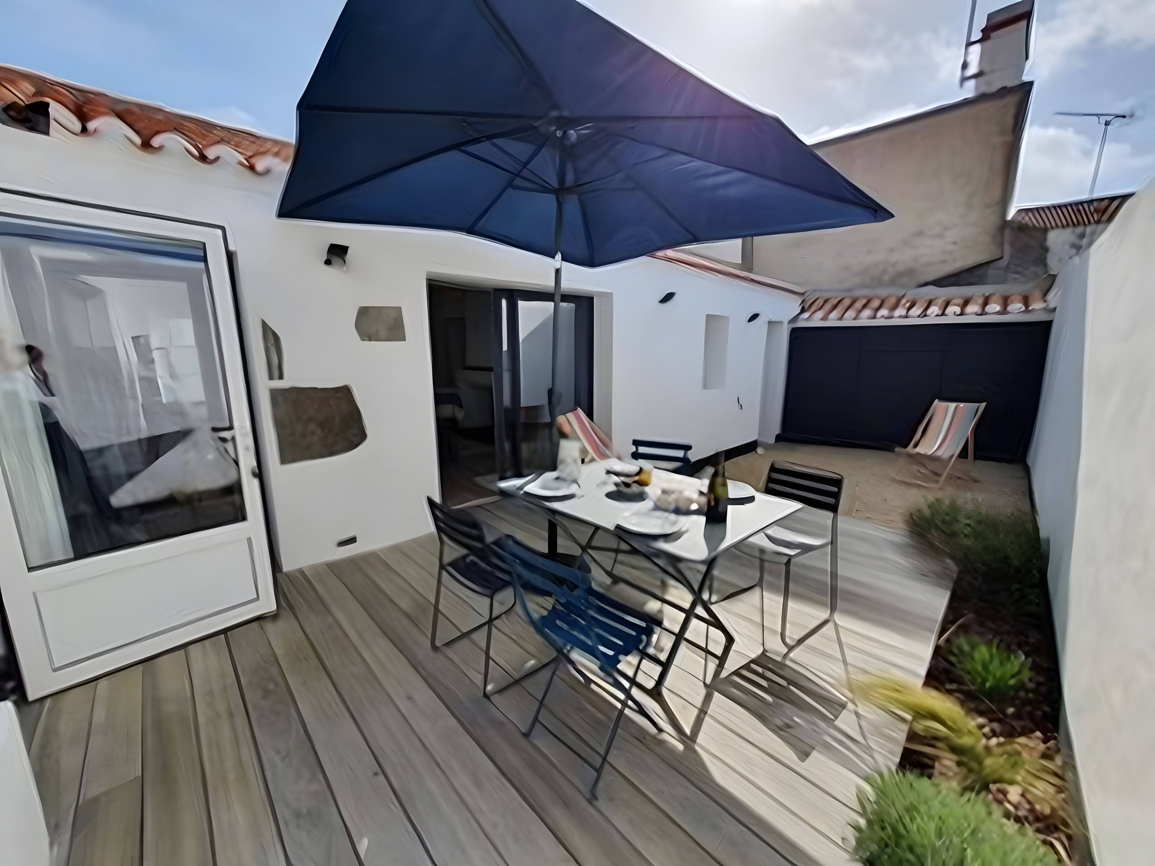 A patio with a table and chairs, a large umbrella, and a view of the sky.