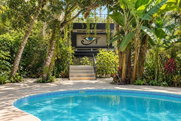 Una piscina rodeada de exuberante follaje y una escalera que conduce a un edificio con un símbolo de ojo.