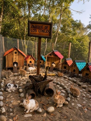 Señal que dice 'PARQUE DE LOS CONEJOS', con jaulas de madera para conejos y animales en un entorno natural.
