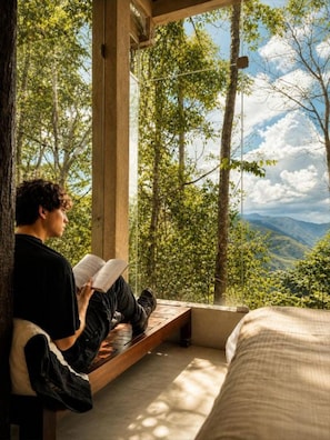 Una persona leyendo un libro en una habitación con vistas a un bosque y montañas.