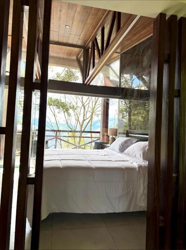 Un dormitorio con cama, vigas de madera en el techo y vistas a árboles y montañas.