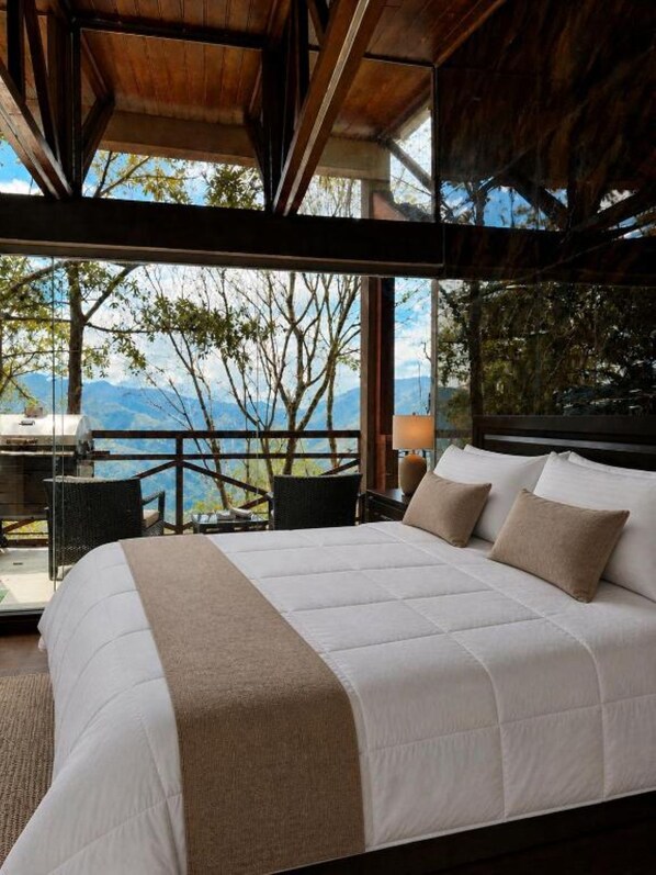 Ein Schlafzimmer mit einem großen Bett, Blick auf Bäume und Berge sowie einem Balkon mit Tisch und Stühlen.
