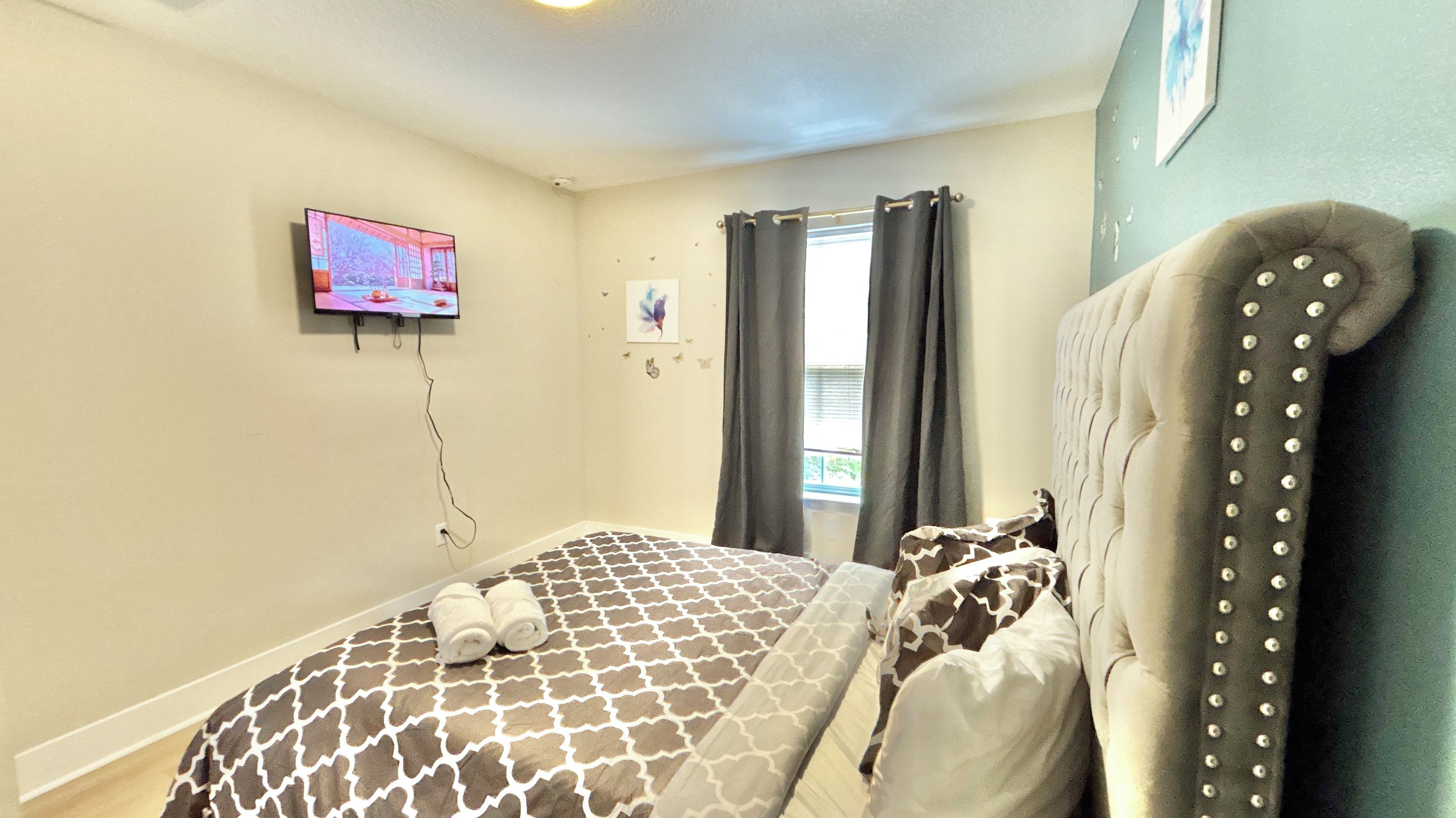 A bedroom with a bed, a television mounted on the wall, and a window with curtains.