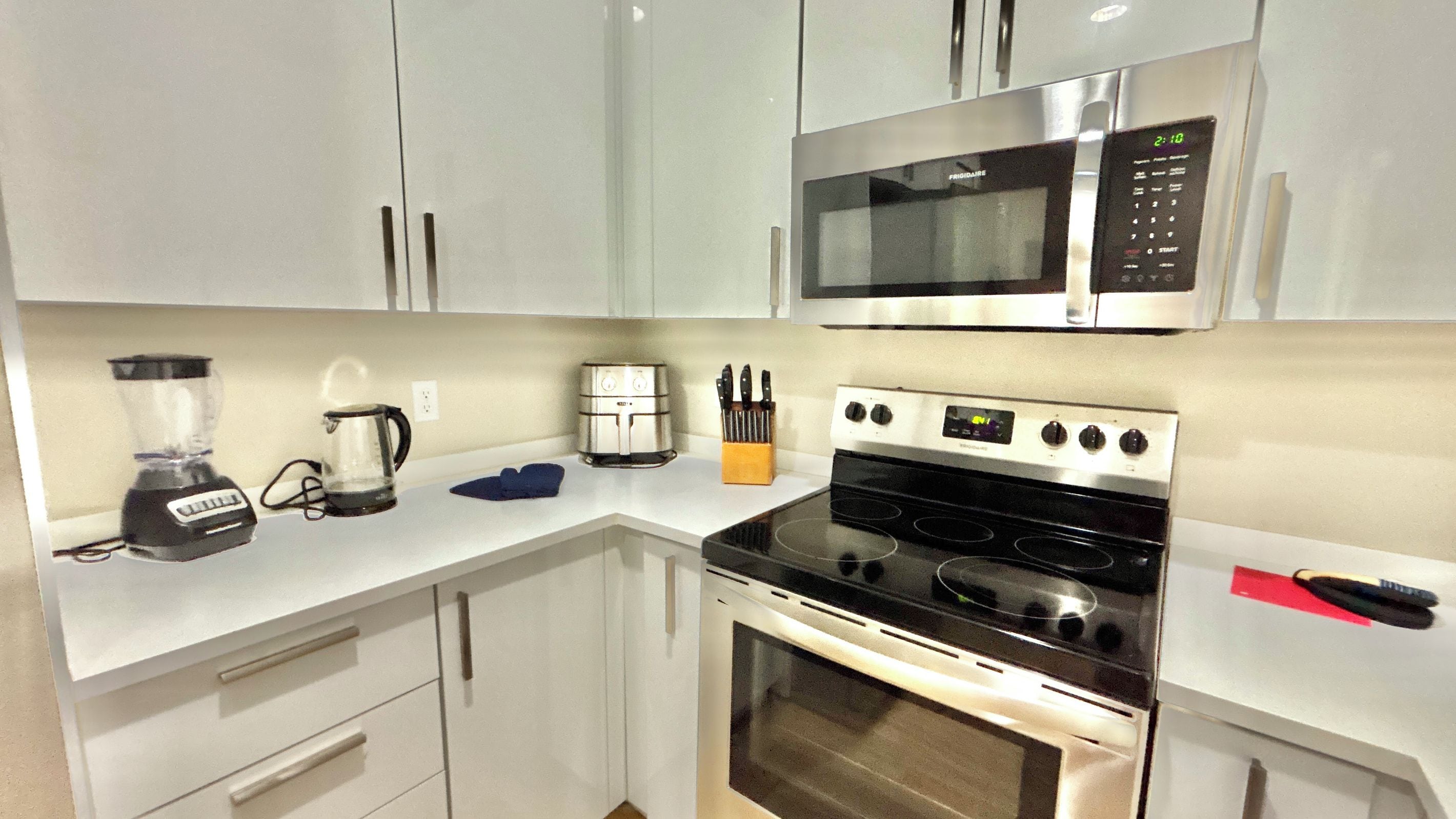 A compact kitchen with a microwave, stove, toaster, blender, and coffee maker.