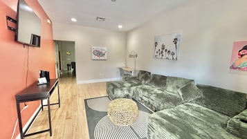 A living room with a sofa, a coffee table, and a TV on the wall.