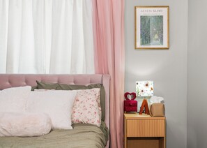 Une chambre à coucher avec un lit, des oreillers, une table de chevet, une lampe et un tableau encadré au mur.