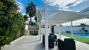 Ein überdachter Außenbereich mit Pool, Sitzgelegenheiten und viel Grün.