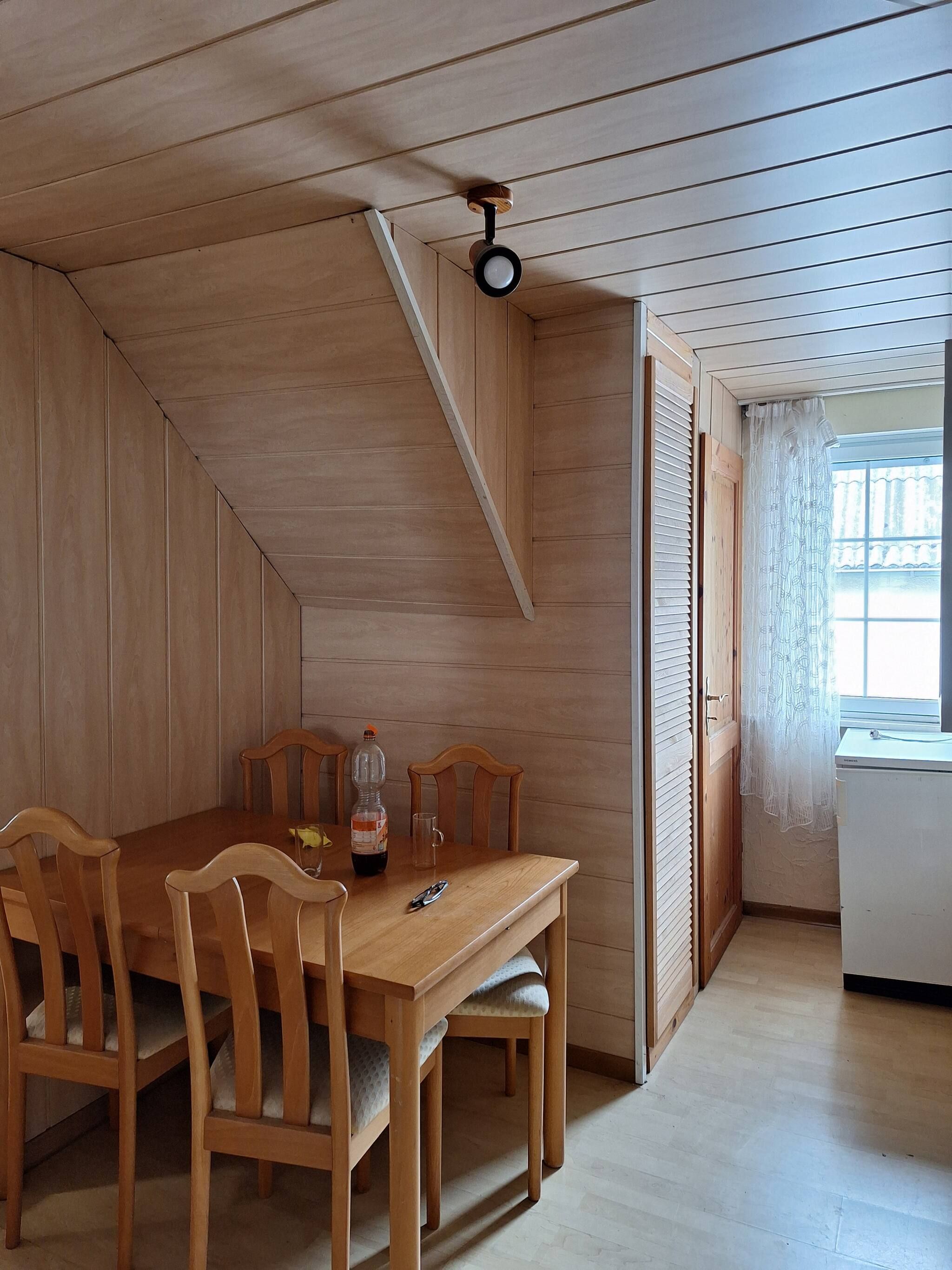 Et værelse med trælofter, et spisebord med stole, en flaske og en kop.