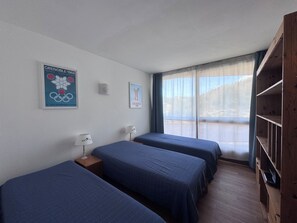 Quarto de hotel com três camas, guarda-roupa de madeira e uma janela com cortinas.