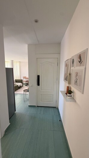 Un passadís amb una porta blanca, una taula petita amb una planta i obra d'art emmarcada a la paret.