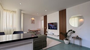 Habitació d'hotel moderna amb zona de menjador, televisió de pantalla plana penjada a la paret, un mirall rodó i una planta en test.