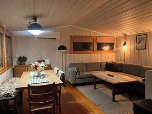 Ein gemütliches Zimmer mit Holzboden, einer Couch, einem Esstisch mit Stühlen und einem kleinen Schrank.
