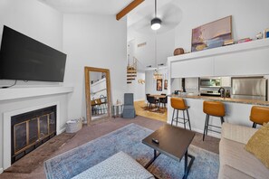 Una sala de estar moderna con televisor de pantalla plana, chimenea, comedor y cocina con taburetes de bar.