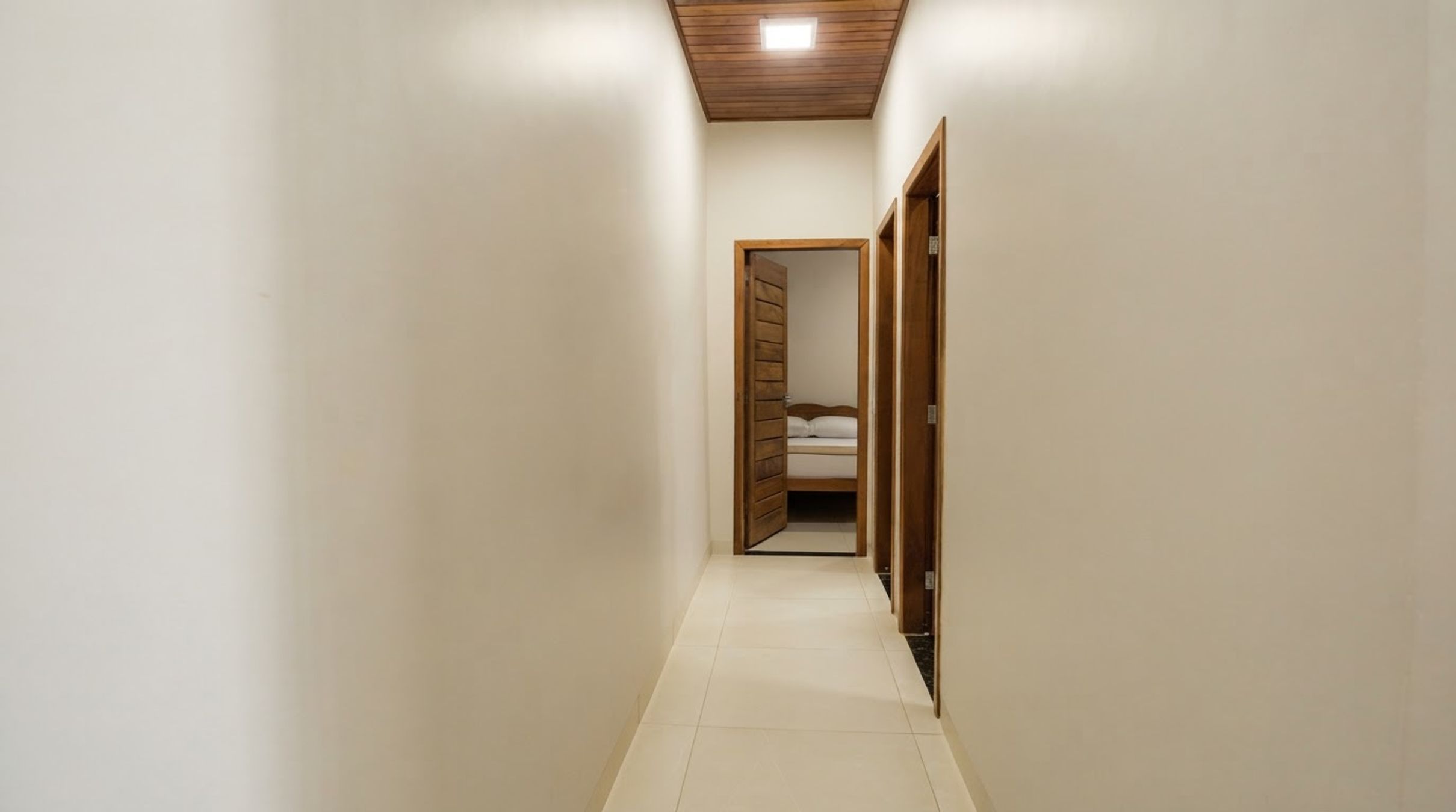 Um corredor estreito com teto de madeira e uma porta que dá para um quarto com cama.