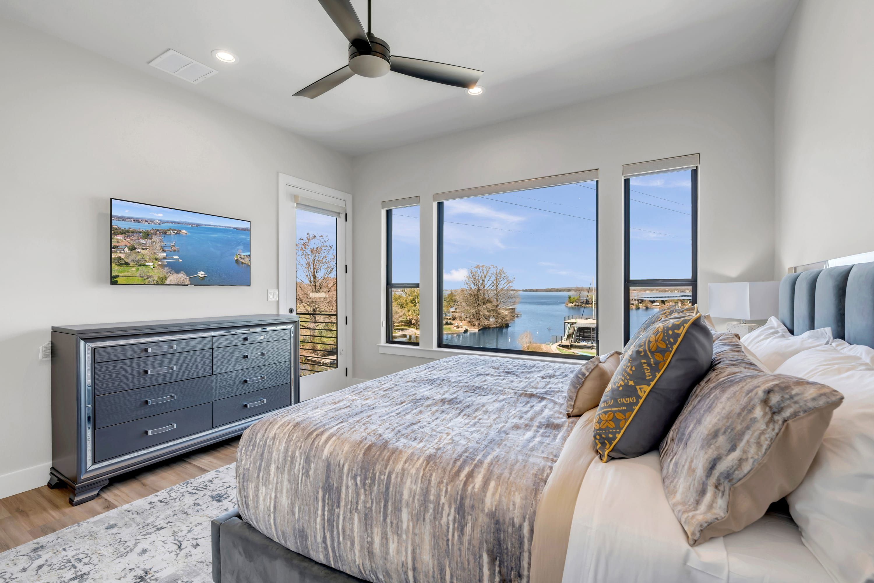 A bedroom with a large bed, a dresser, a ceiling fan, and a TV.