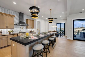 Een moderne keuken met een groot eiland, barkrukken, hanglampen en uitzicht op buiten.